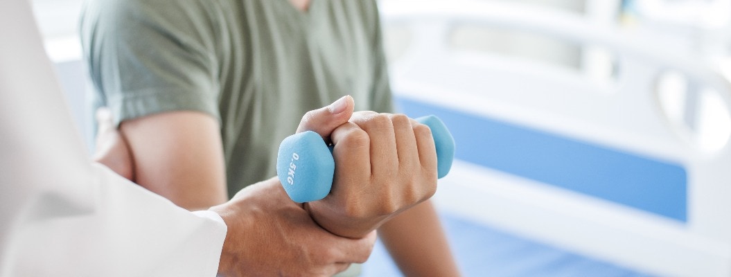 Zwei Personen bei der Physiotherapie: Eine Person mit einem Gewicht in der Hand