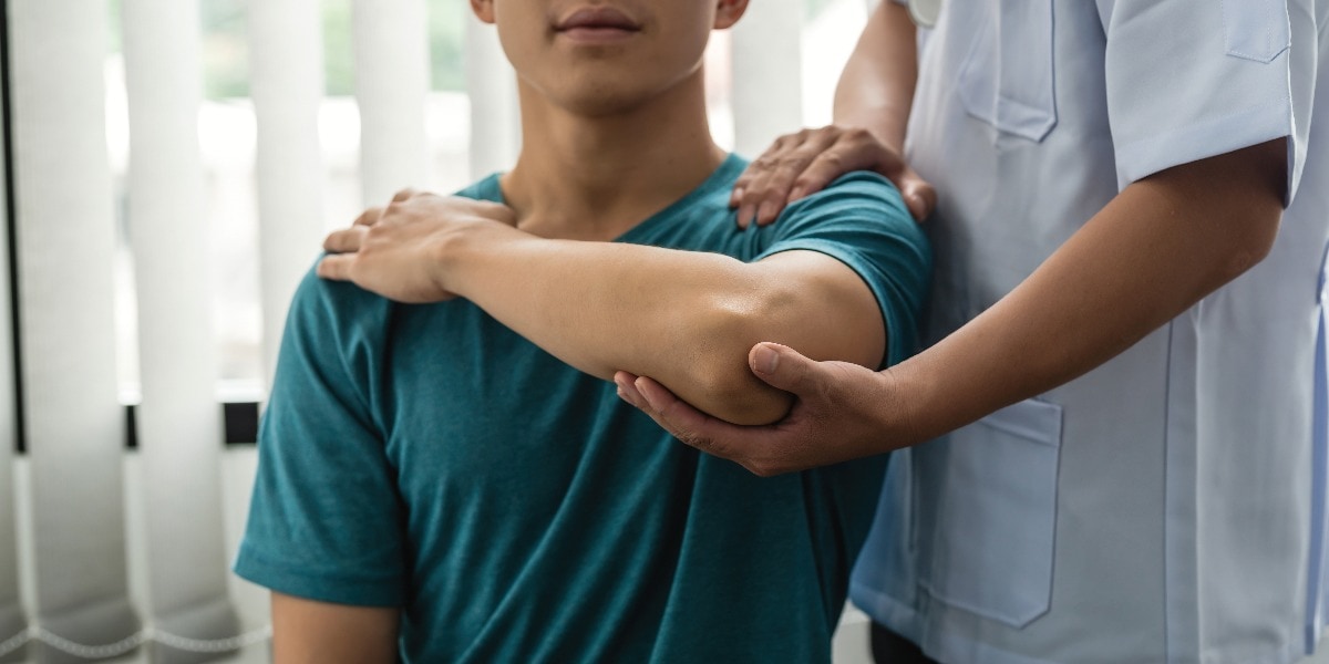 Physiotherapeut hilft einem Patienten mit einer Ellenbogenverletzung