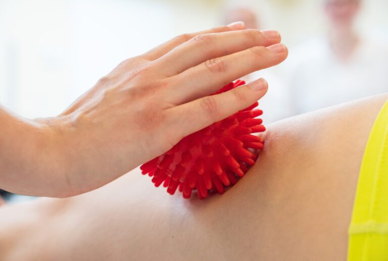 Eine weibliche Person massiert mit Hilfe eines roten Massageballs den Rücken einer Frau