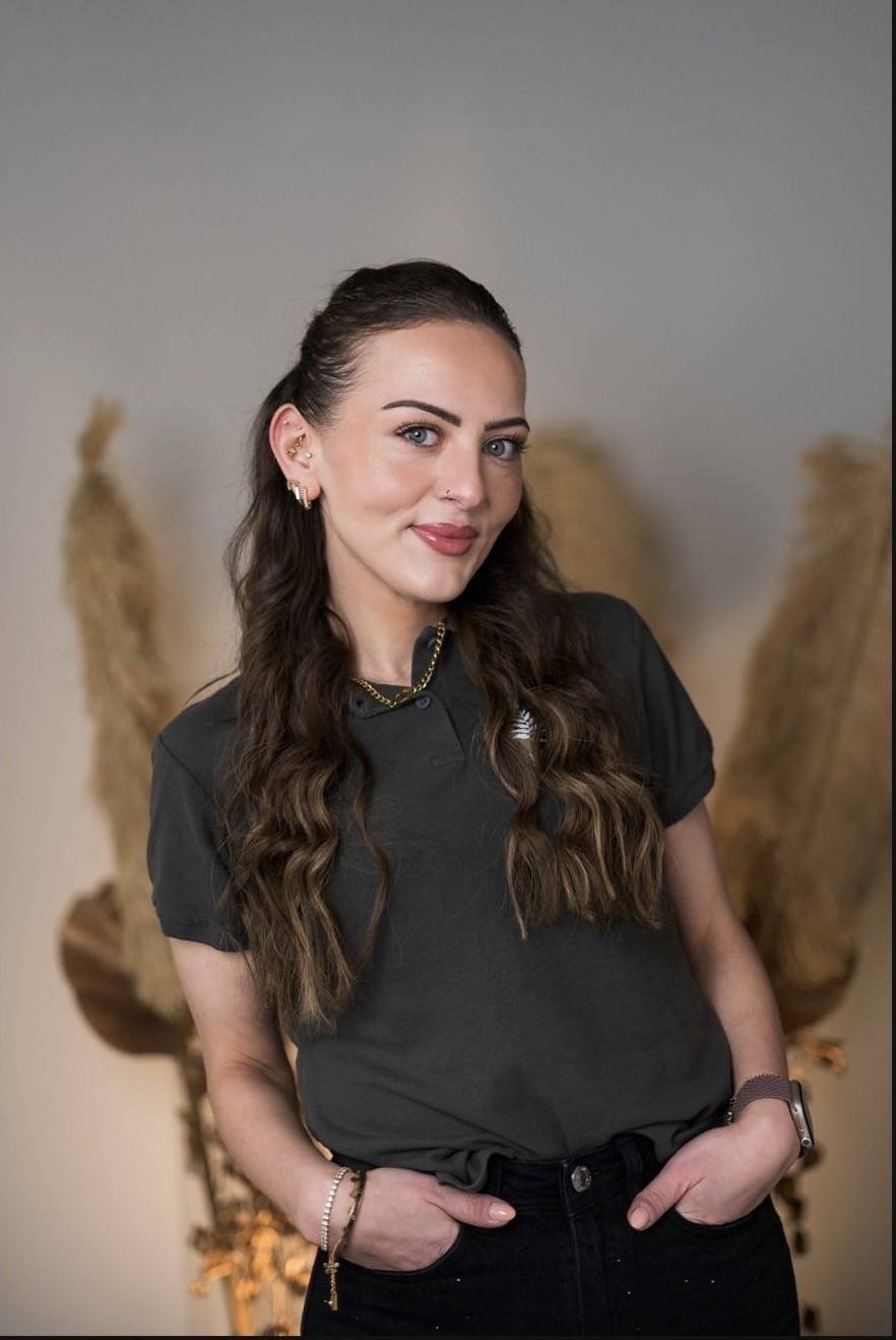 Eine Frau mit langen braunen Haaren lächelt. Sie trägt ein schwarzes T-Shirt. Hintergrund ist dezent.