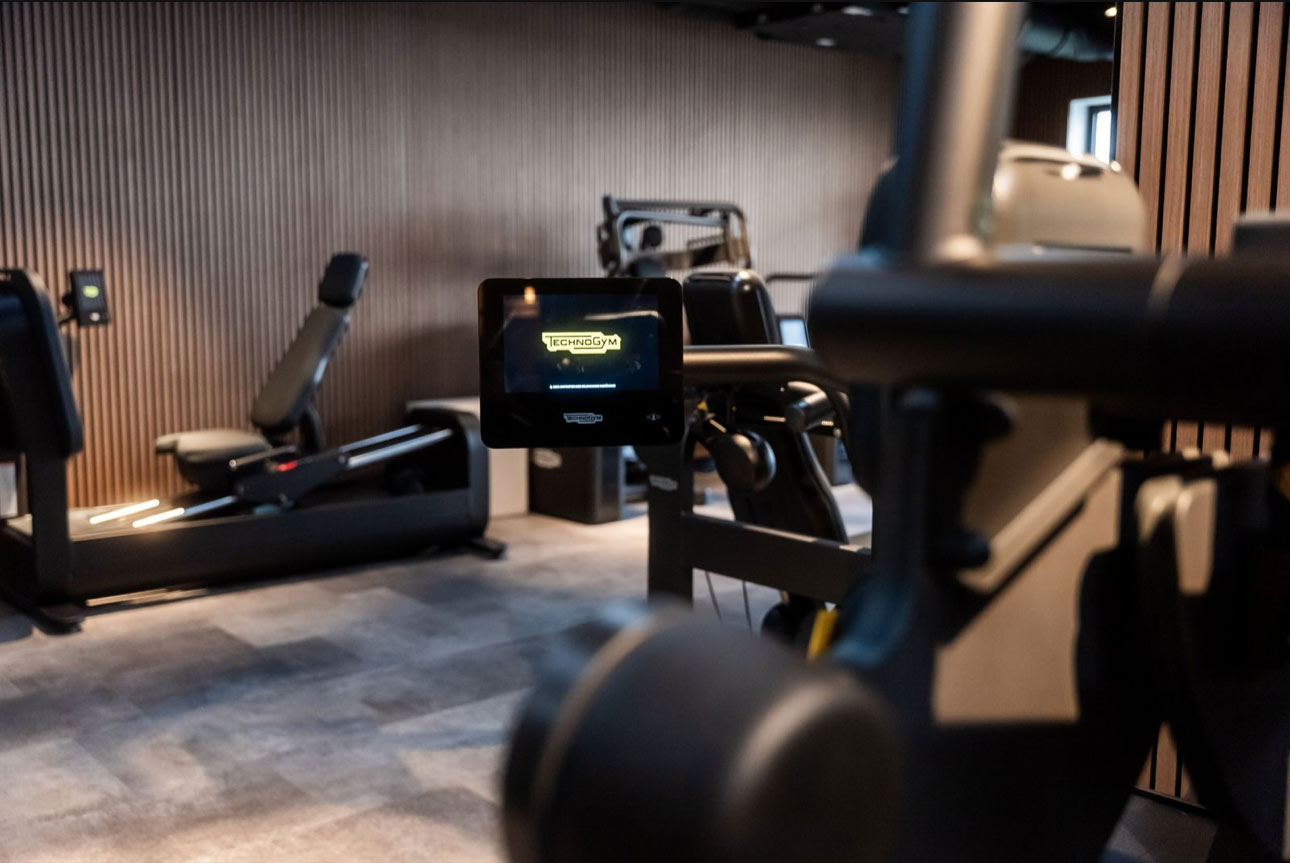 Fitnessstudio mit modernen Geräten und grauem Boden, Fokus auf Bildschirm mit gelbem Logo.