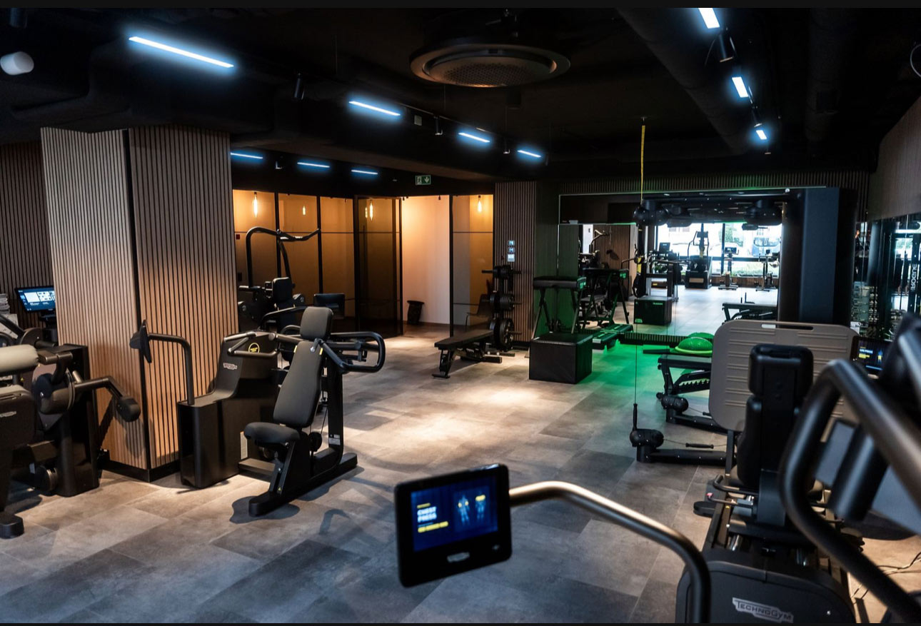 Ein moderner Fitnessraum mit Geräten, Spiegel, gedämpftem Licht und grüner Beleuchtung.