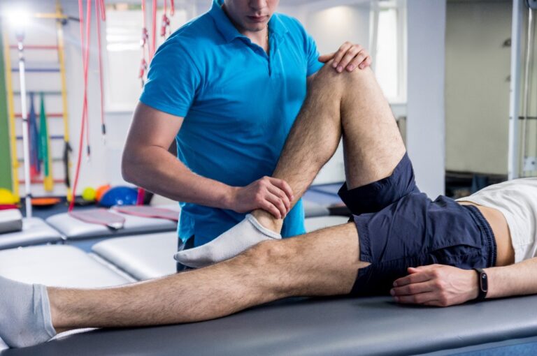Rehabilitationstherapie. Physiotherapeutin bei der Arbeit mit einem jungen männlichen Patienten im Rehabilitationszentrum