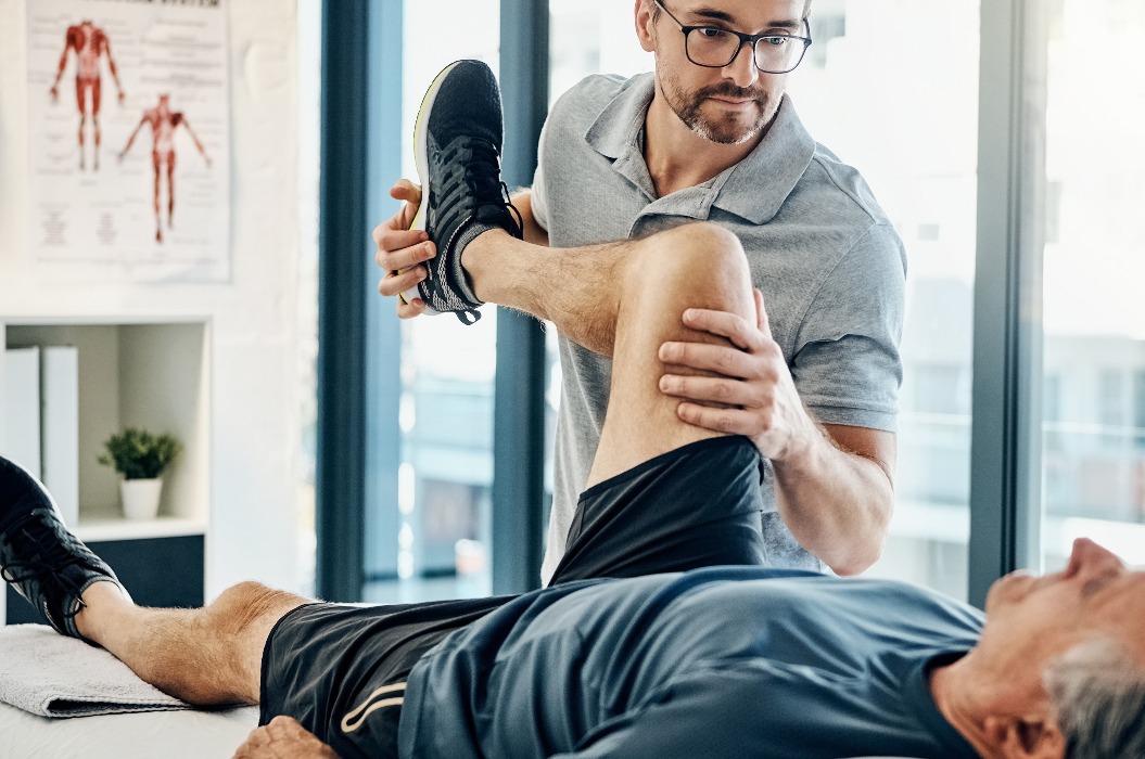 Stretching Beine, Rehabilitation und ein Physiotherapeut mit einem Mann für Wellness und Behinderung Unterstützung. Hilfe, Gesundheit und ein männlicher Arzt, der einer älteren Person bei der Physiotherapie der Körpermuskulatur hilft