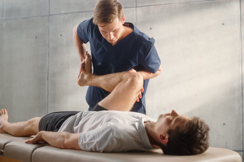 Fortgeschrittene Sportphysiotherapeutin beim Dehnen und Arbeiten an Muskelgruppen oder Gelenken mit einem jungen männlichen Athleten. Ein fitter Sportler, der sich von einer leichten Verletzung erholt und sich in der Rehabilitation befindet.