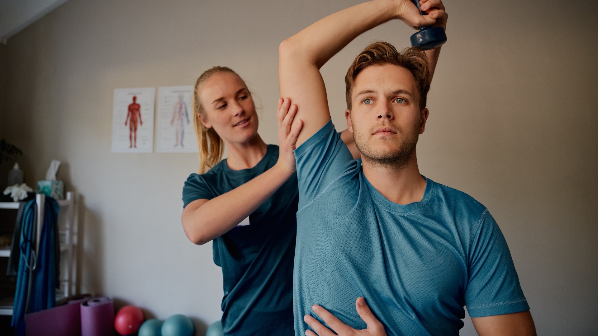 Eine junge Physiotherapeutin unterstützt einen Patienten beim Heben von Hanteln in einem Rehabilitationszentrum.