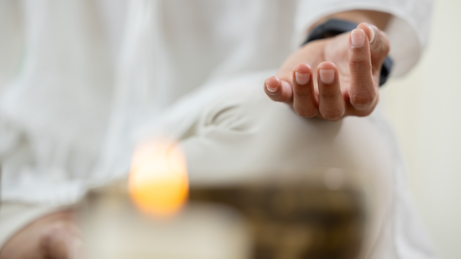 Eine achtsame Frau in weißer Kleidung sitzt da und macht eine Handgeste für eine Meditations- und Heilungssitzung mit tibetischer Klangschale und Kerze, die eine friedliche, ruhige, entspannende und energetische Atmosphäre schafft