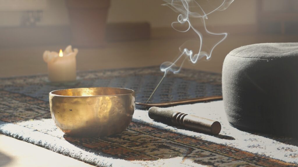 Meditationsraum mit Klangschale, Räucherstäbchen, Rauch, Kissen und Kerze
